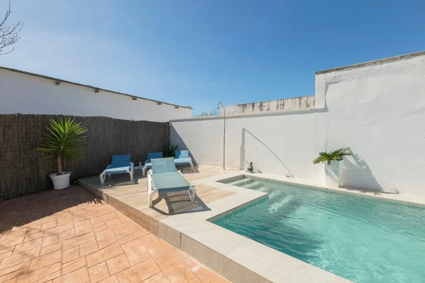 An outdoor swimming pool beside a tiled patio with lounge seating.