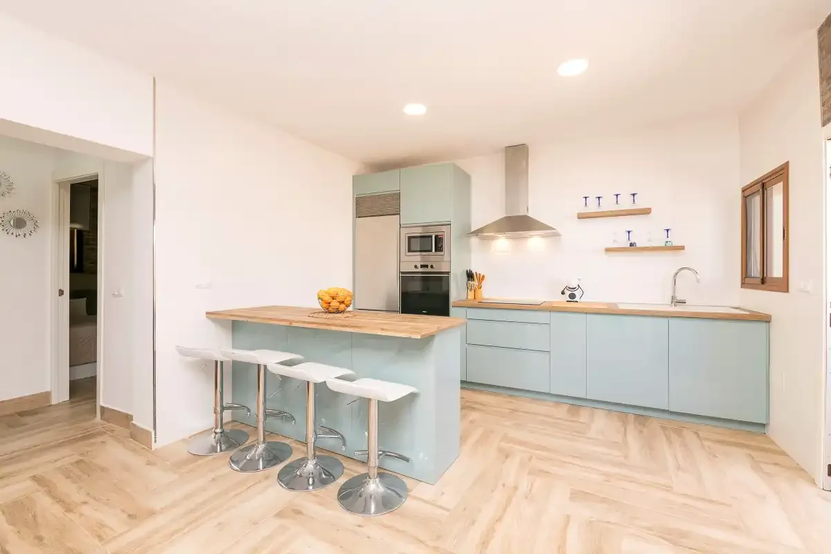 A bright kitchen has pale blue cabinets and a wooden breakfast bar.