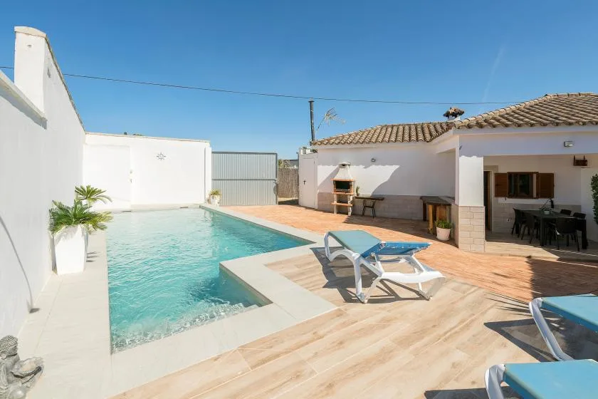 An outdoor swimming pool sits beside a tiled patio and a white building.