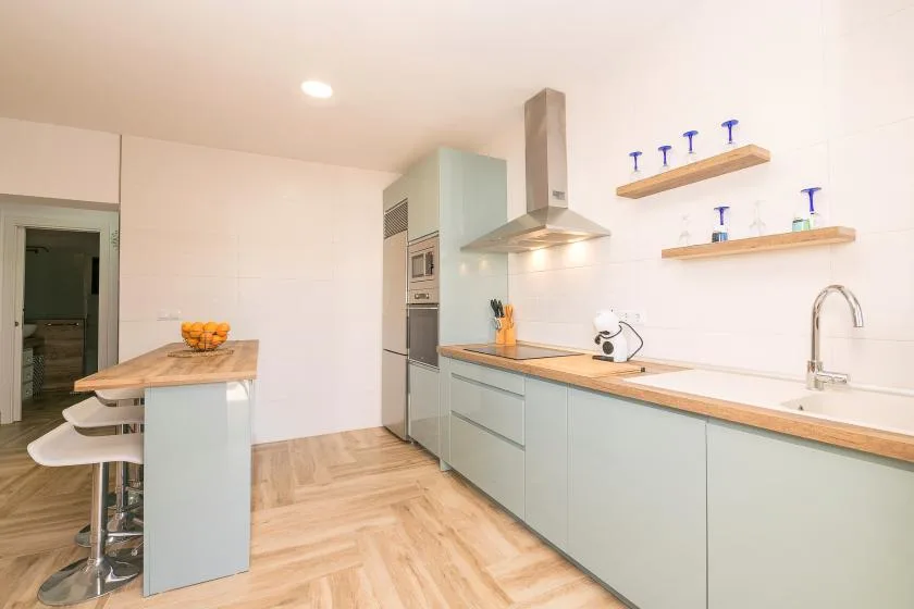 A bright modern kitchen with pale cabinetry, a wooden countertop, and a central island.