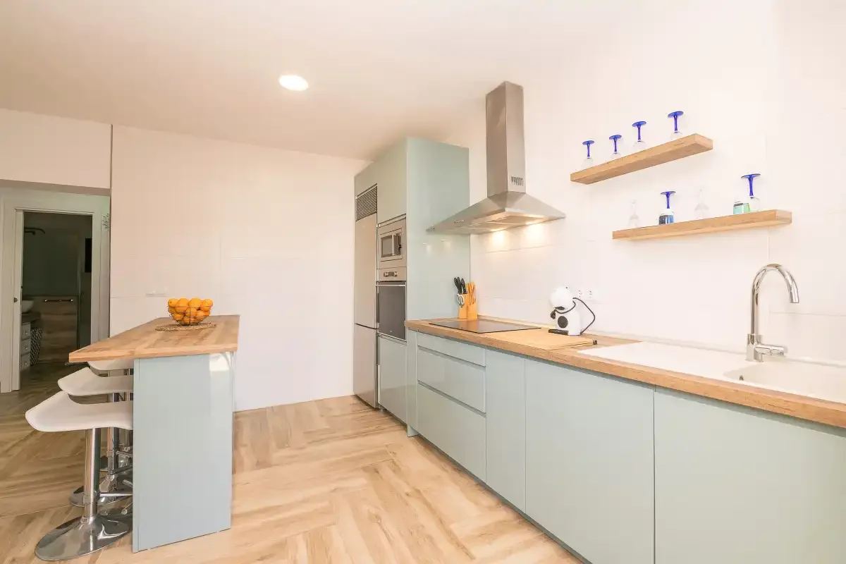 A bright modern kitchen with pale cabinets, a central island, and a long countertop.