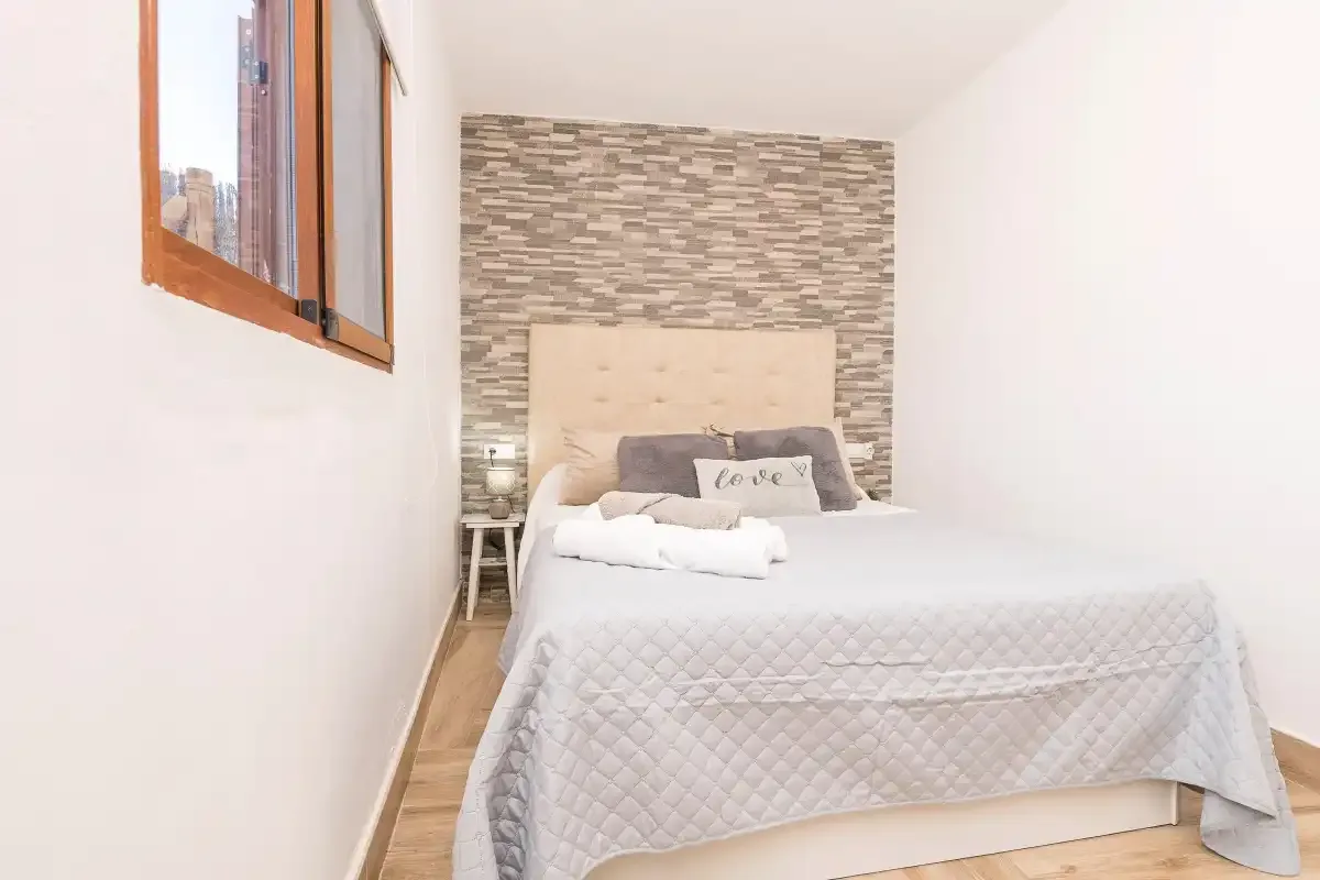 A bedroom with a neatly made bed and a patterned accent wall.