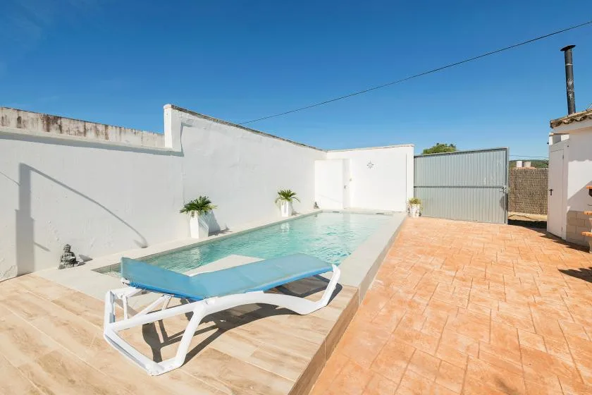 An outdoor swimming pool sits beside a sunlit tiled patio.