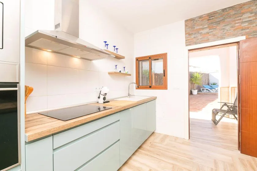 A modern kitchen with pale cabinets, a wooden countertop, and a cooktop.