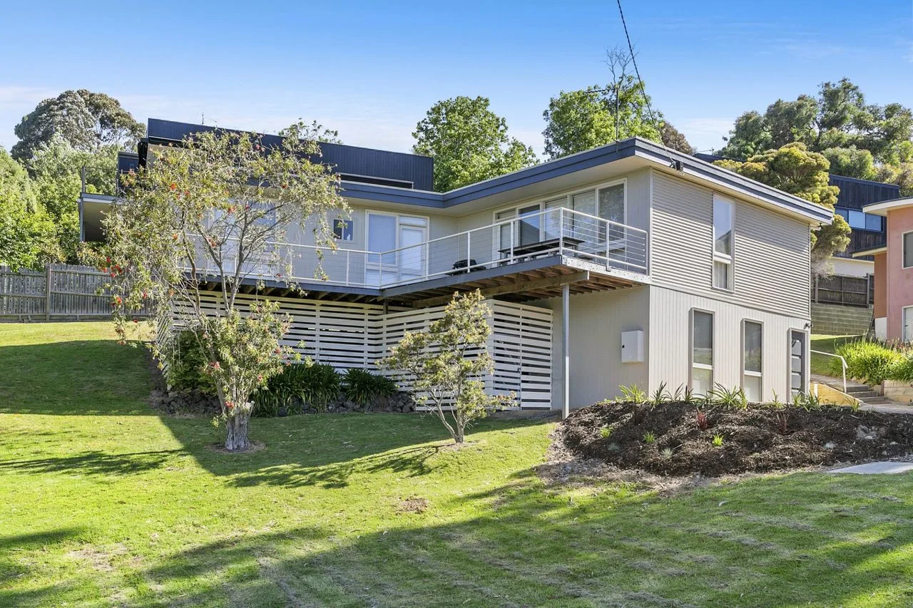 Una casa moderna con una terraza elevada da a un césped verde.