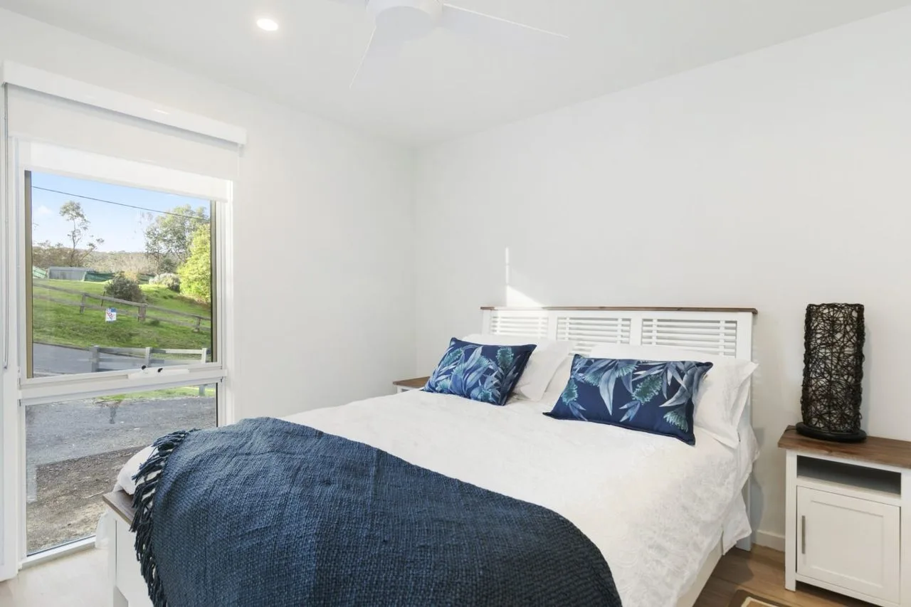 Un dormitorio luminoso con ropa de cama blanca y una gran ventana con vistas a la vegetación.