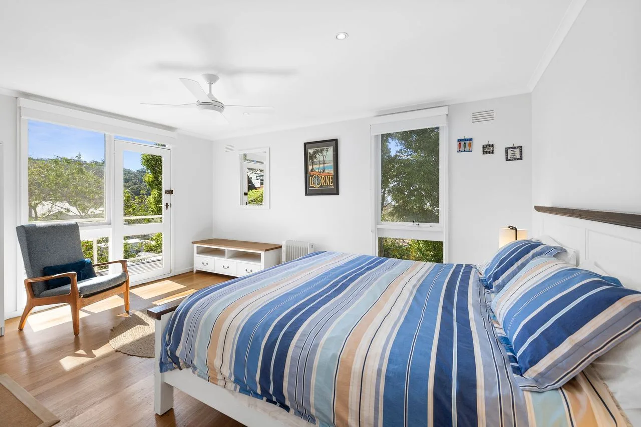 Un dormitorio luminoso con una cama y una silla junto a grandes ventanas.