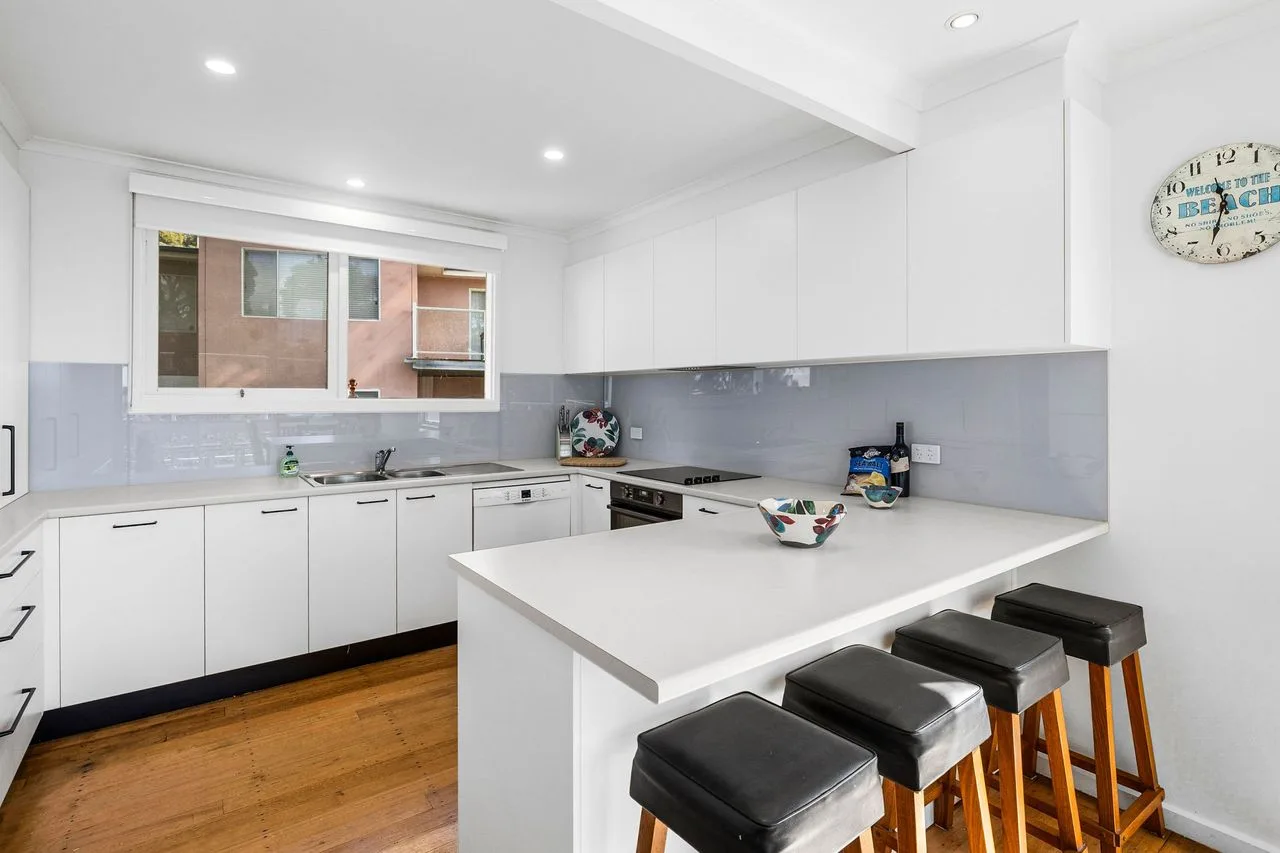 Una cocina blanca y luminosa con isla y asientos de barra.