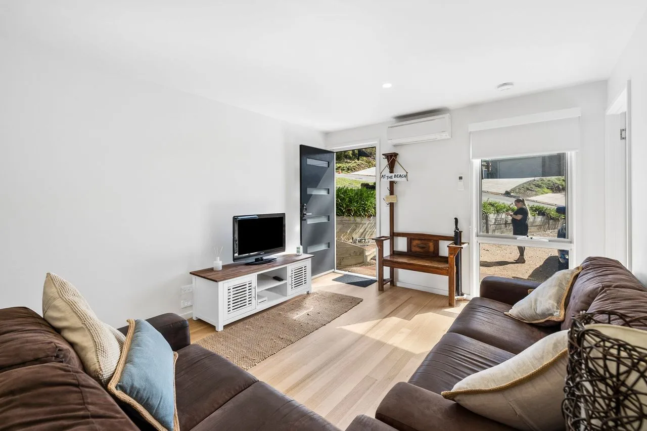 Sala de estar con asientos, un televisor y puertas de vidrio abiertas hacia el exterior.
