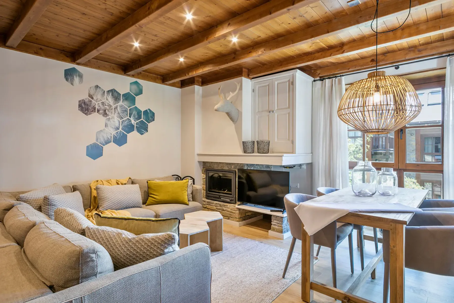 A living room with a sectional sofa, television, and dining table beneath a wooden ceiling.