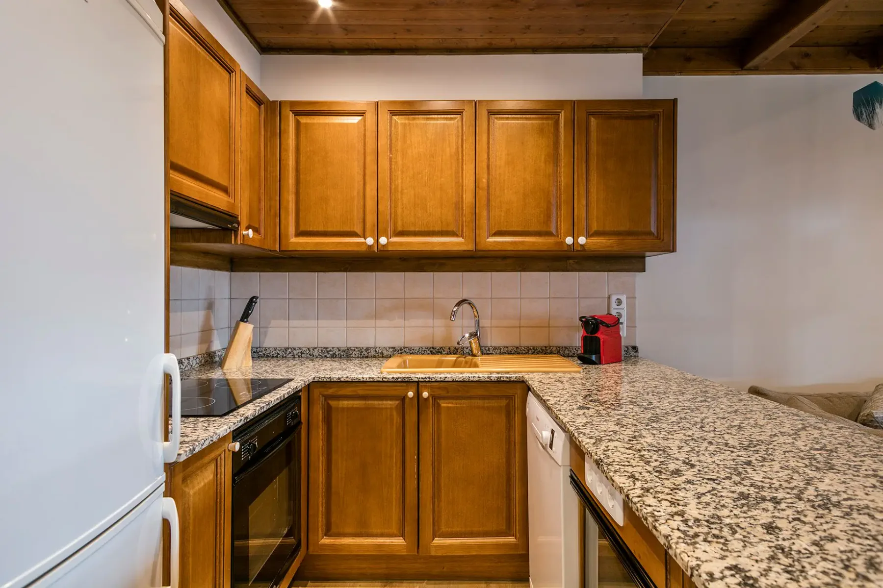 A compact kitchen with wooden cabinetry, tiled walls, and a speckled countertop.