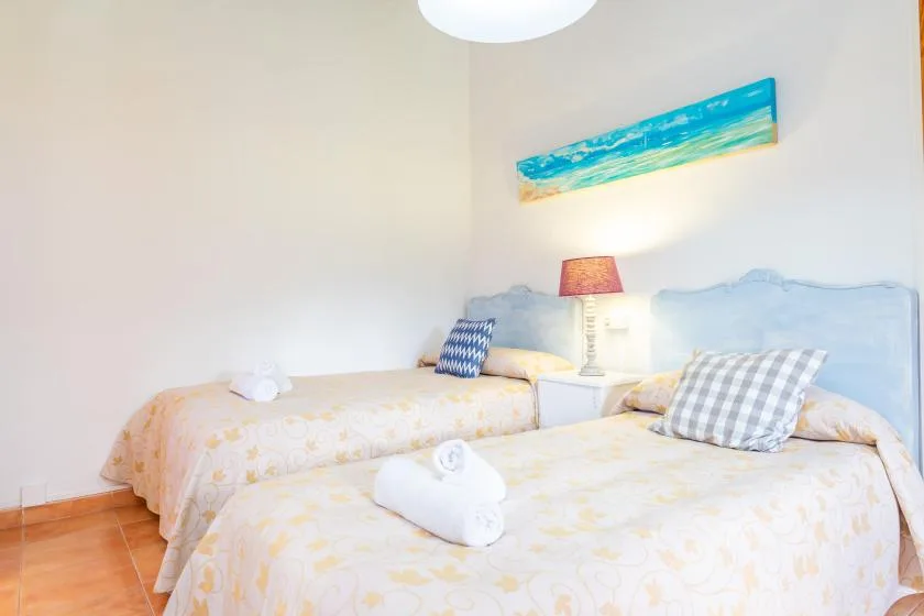 A bright bedroom with two beds, patterned bedding, and a lamp between them.