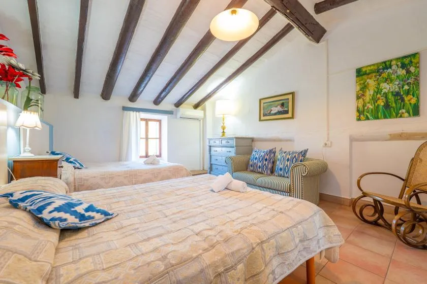 A bedroom with two beds, a small seating area, and exposed ceiling beams.