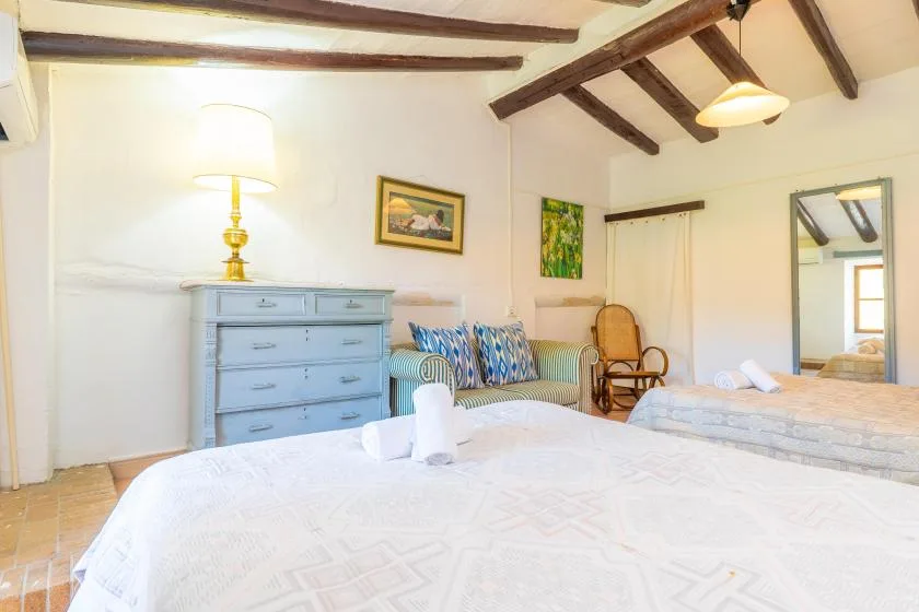 A bedroom with a large bed, a blue dresser, and exposed ceiling beams.