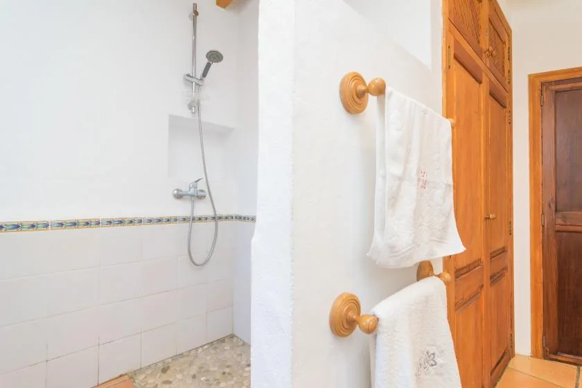 A tiled bathroom with a wall-mounted shower and towels hanging beside a wooden door.
