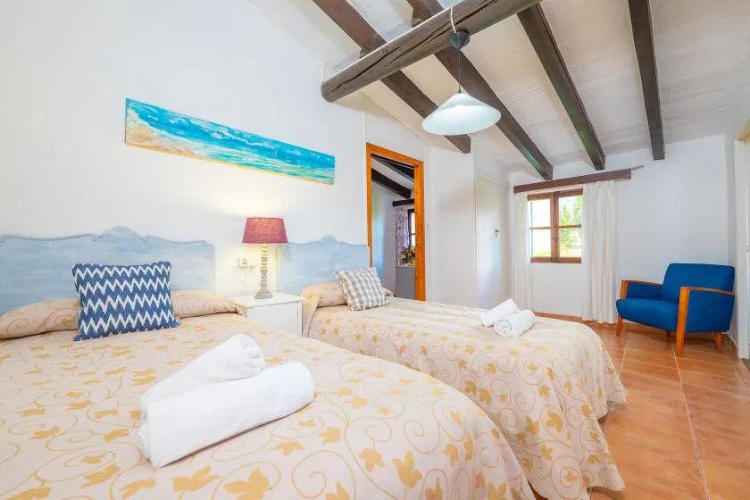 A bedroom with two beds, folded towels, and a blue armchair.