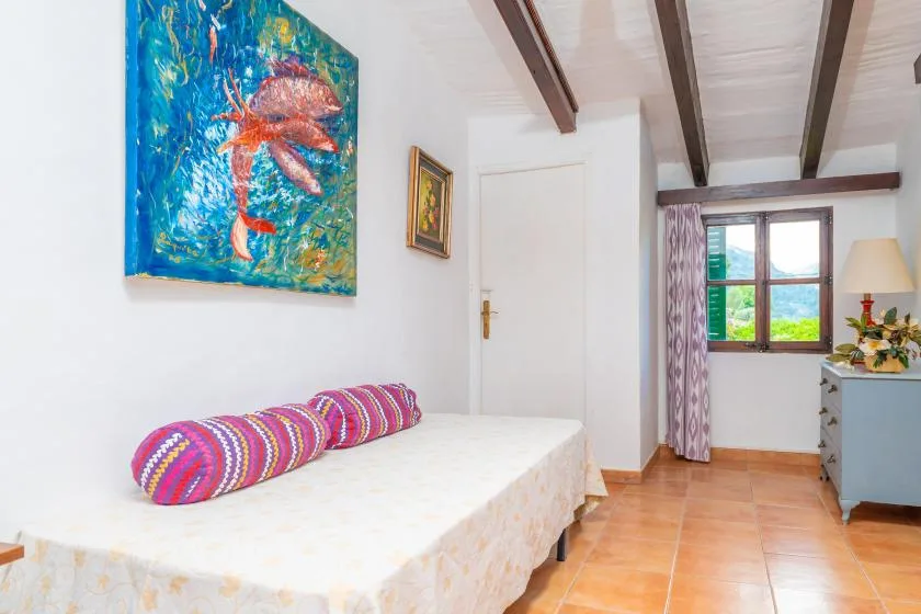A bedroom with a single bed, colorful artwork, and a window overlooking greenery.