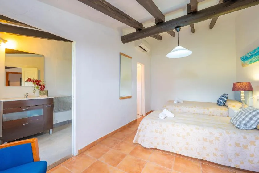 A bedroom with two beds, exposed ceiling beams, and a tiled floor.