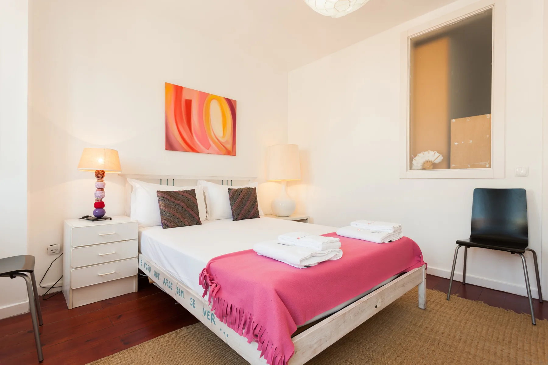 Un dormitorio luminoso con una cama cubierta con una manta rosa y toallas dobladas.