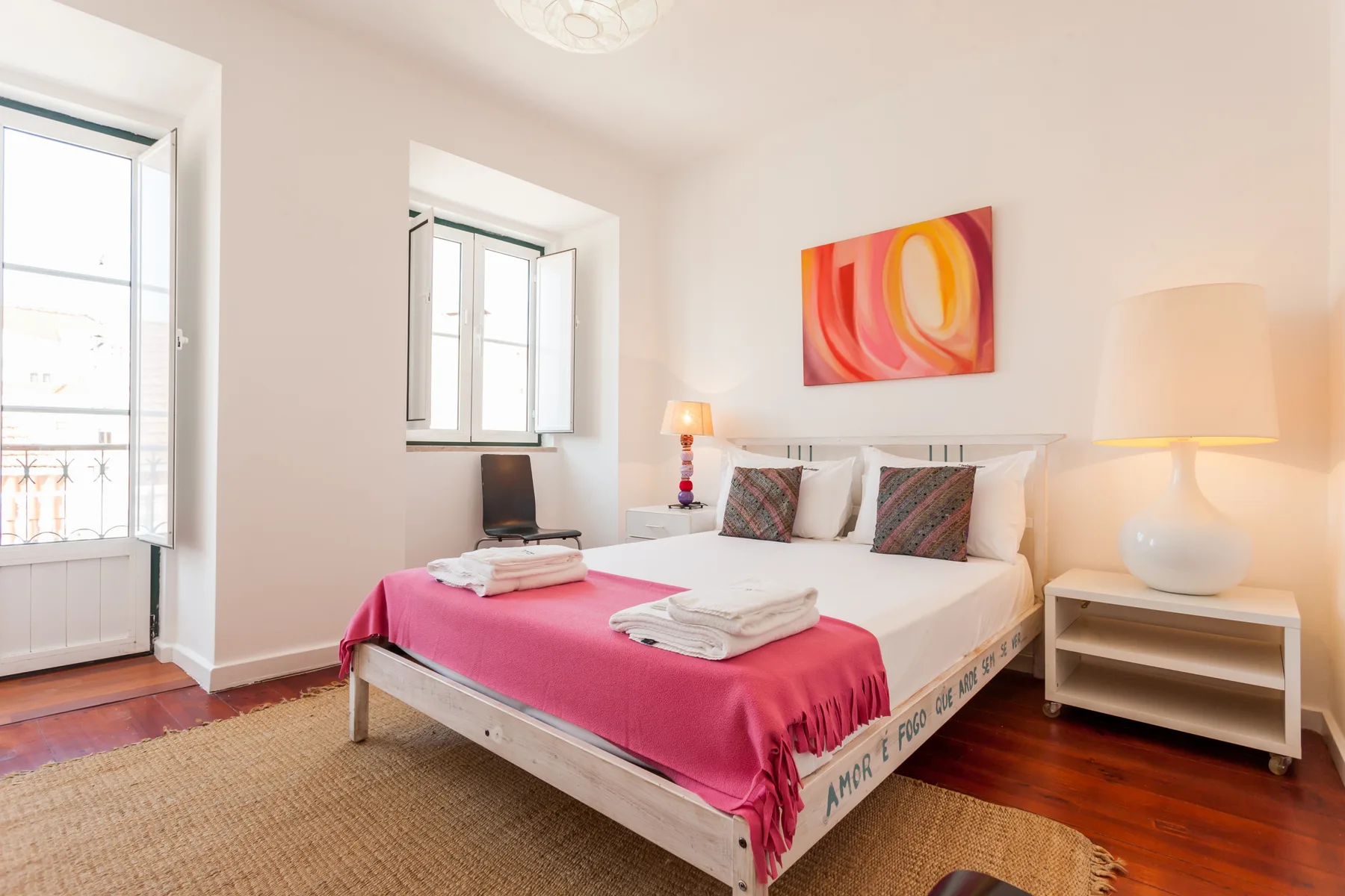 Un dormitorio luminoso con una cama doble, una colcha rosa y arte colorido en la pared.