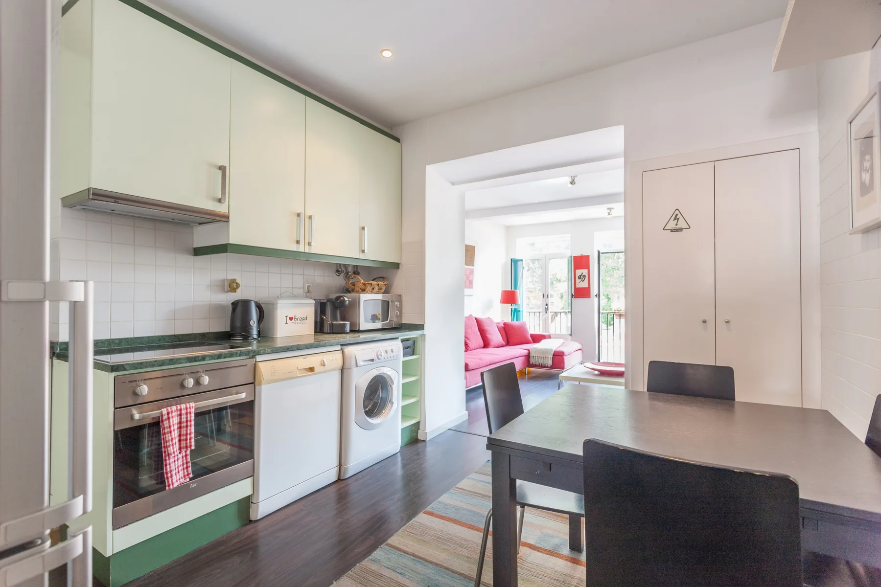 Una cocina compacta se abre a un comedor y una sala luminosa con asientos rosados.