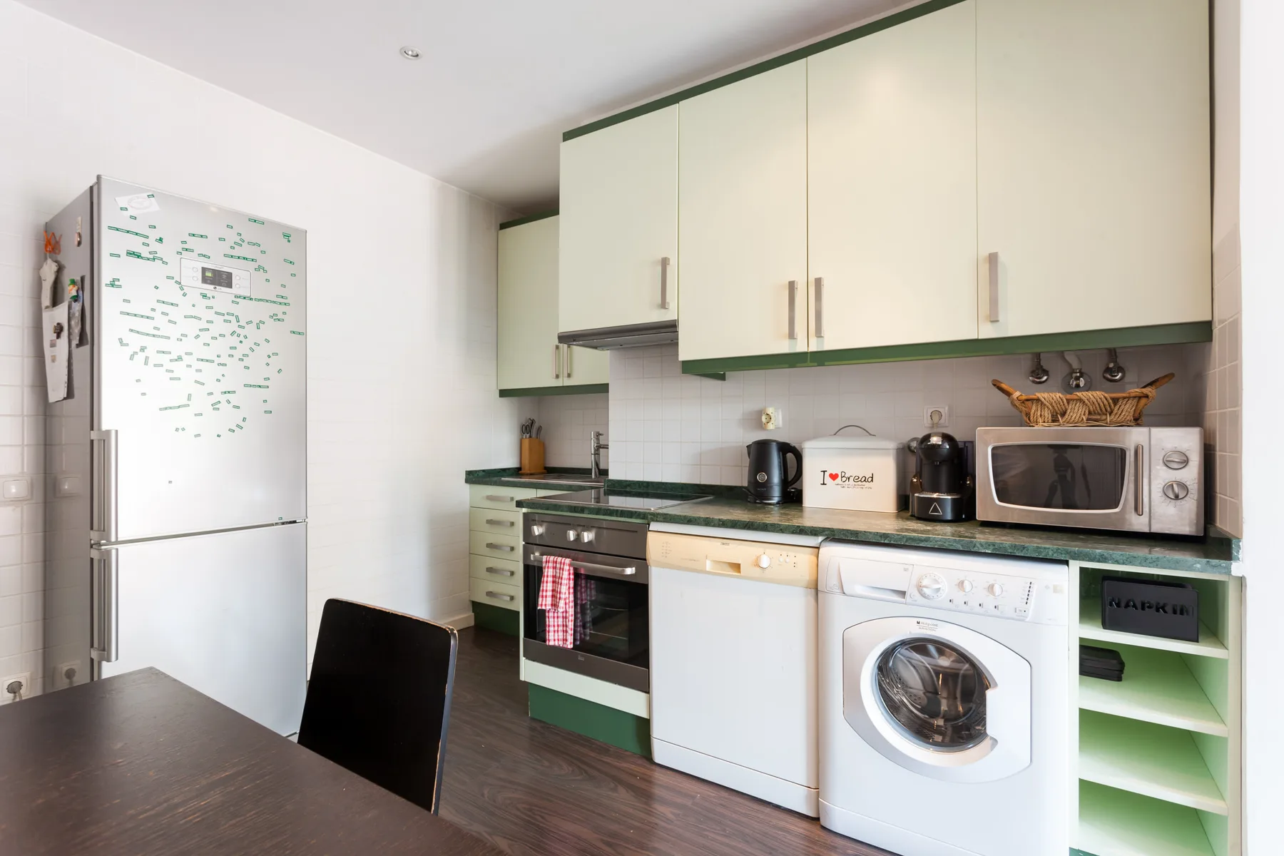 Una cocina compacta con armarios claros, un refrigerador y electrodomésticos de lavandería.