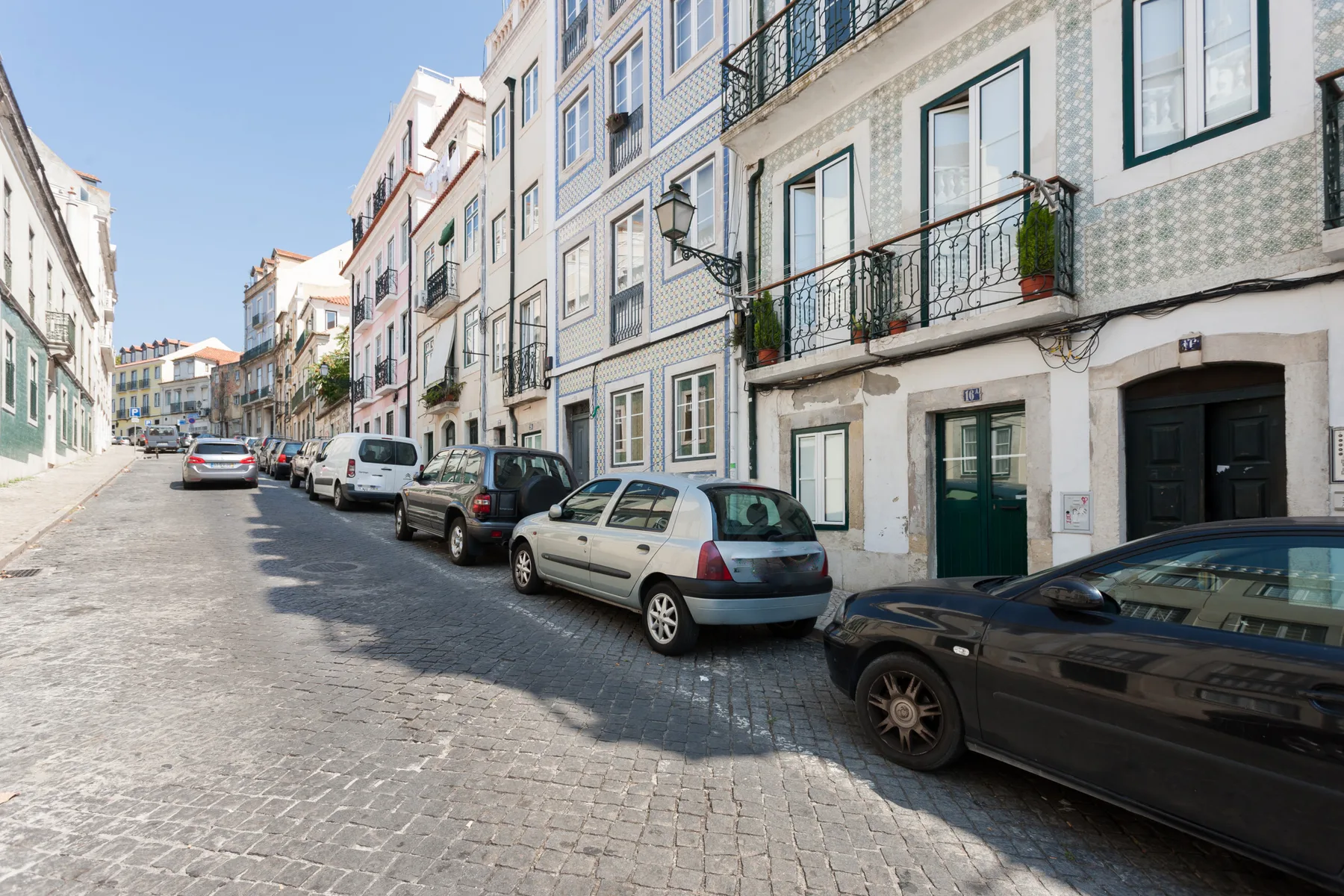 Una calle empedrada flanqueada por edificios de varias plantas y coches aparcados.