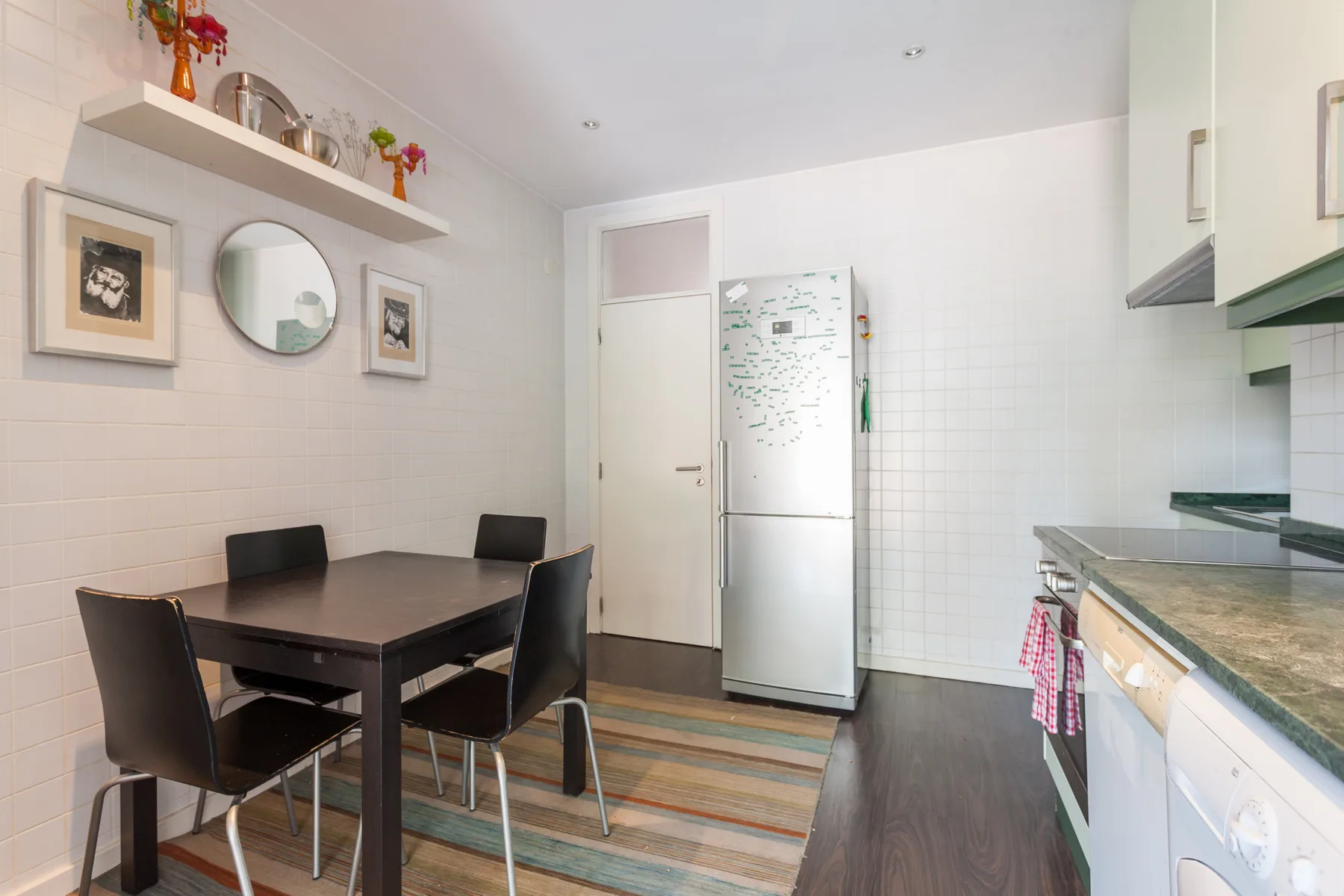 Una cocina luminosa con comedor y una mesa junto al refrigerador.
