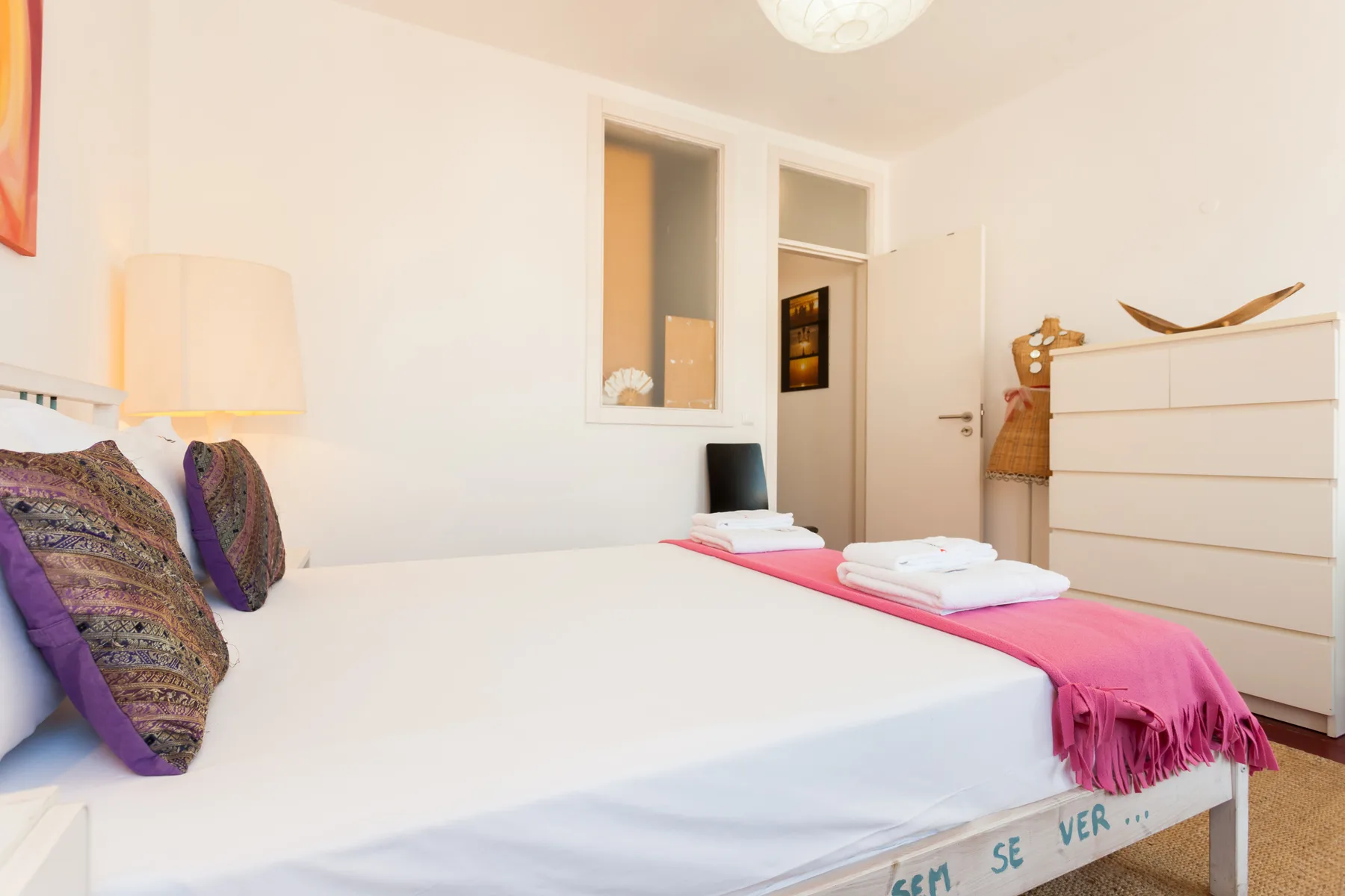 Un dormitorio con una cama vestida con ropa blanca y una manta rosa.