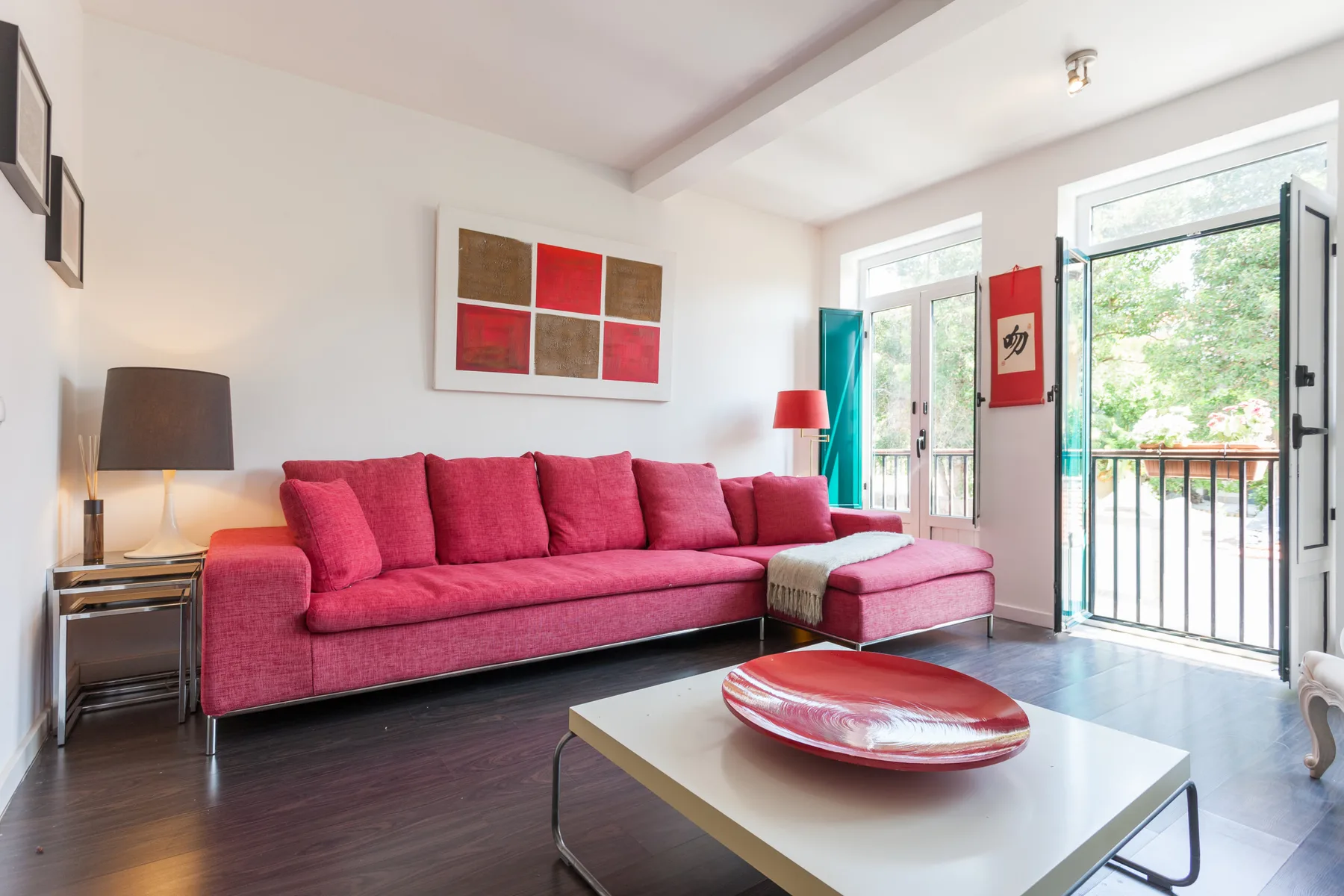 Una sala de estar luminosa con asientos rosas y puertas de vidrio hacia un balcón.