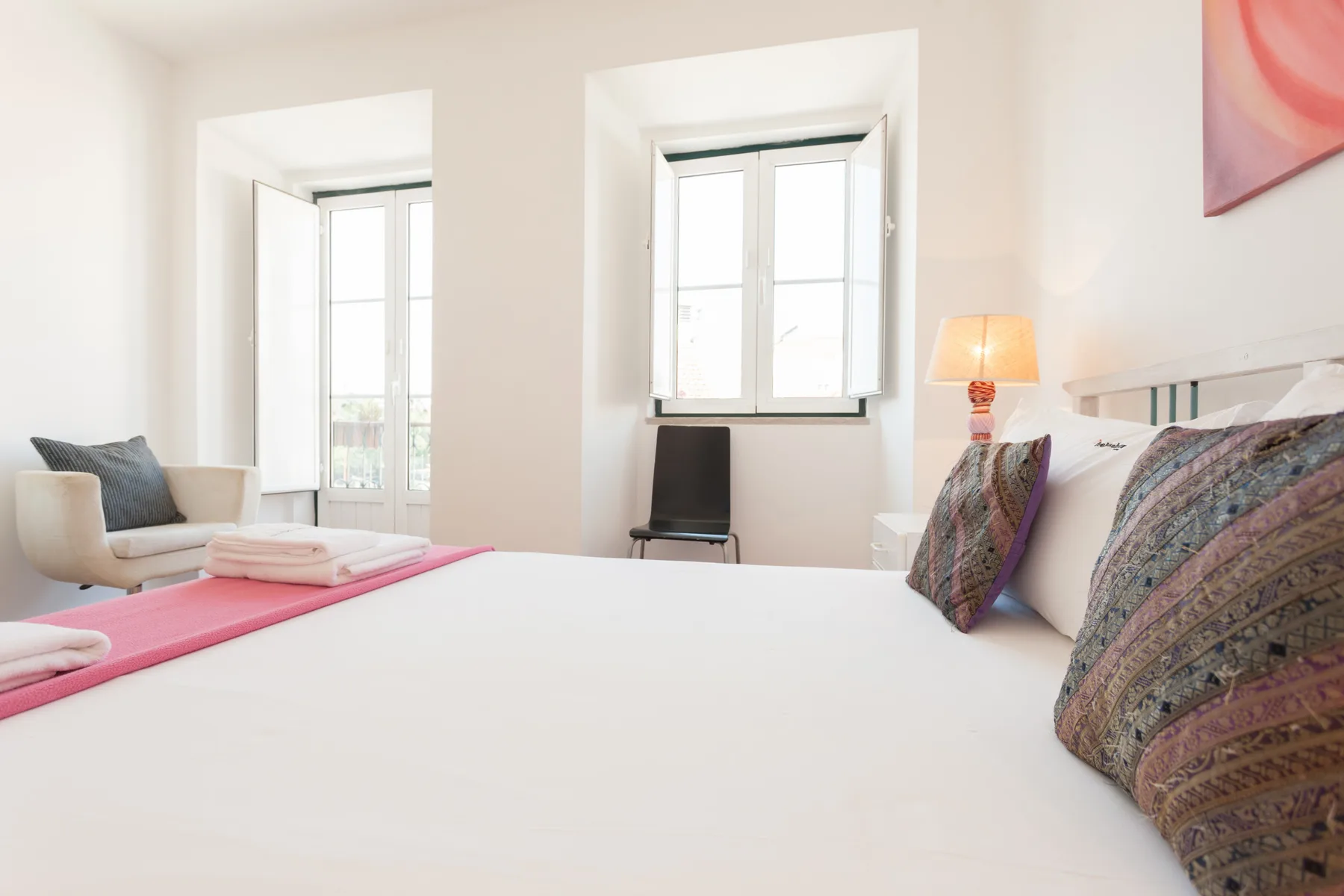 Un dormitorio luminoso con una cama grande y ventanas altas.