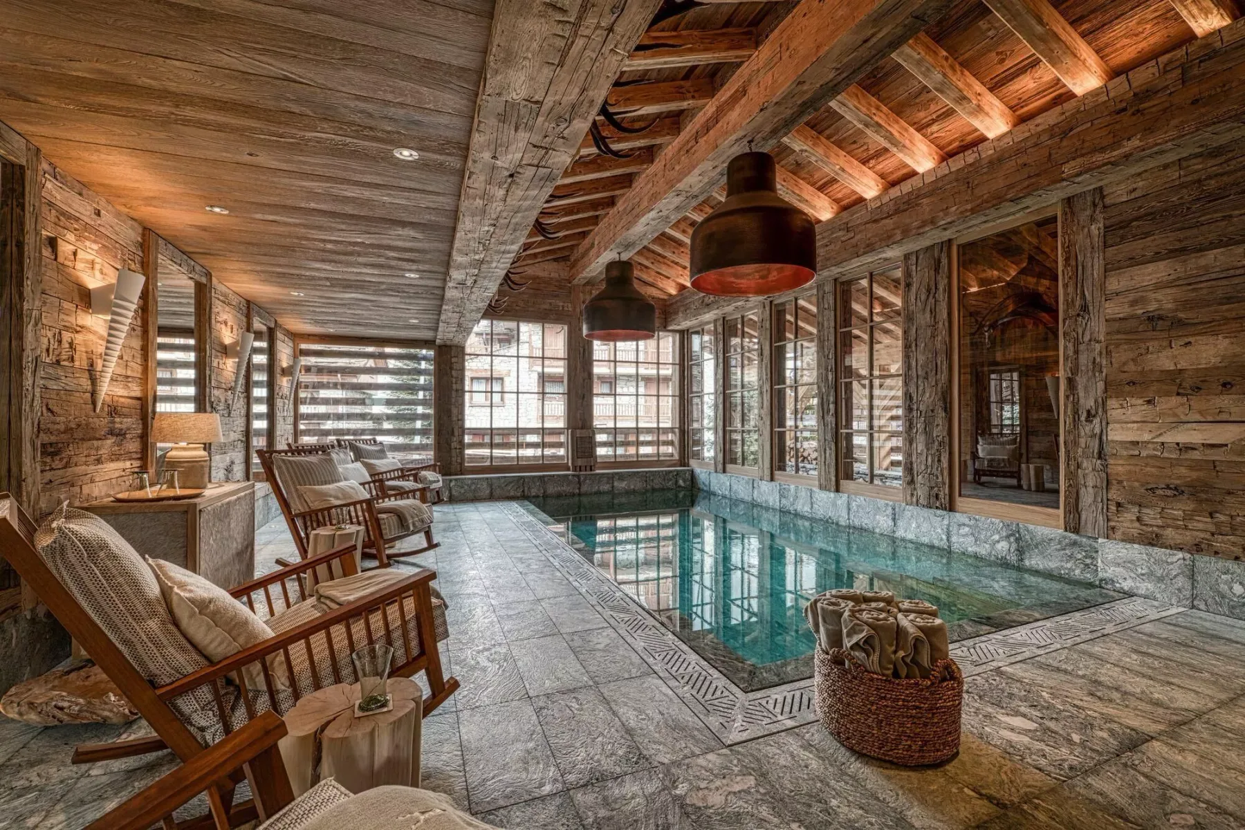 An indoor swimming pool sits beside wooden seating and large windows.