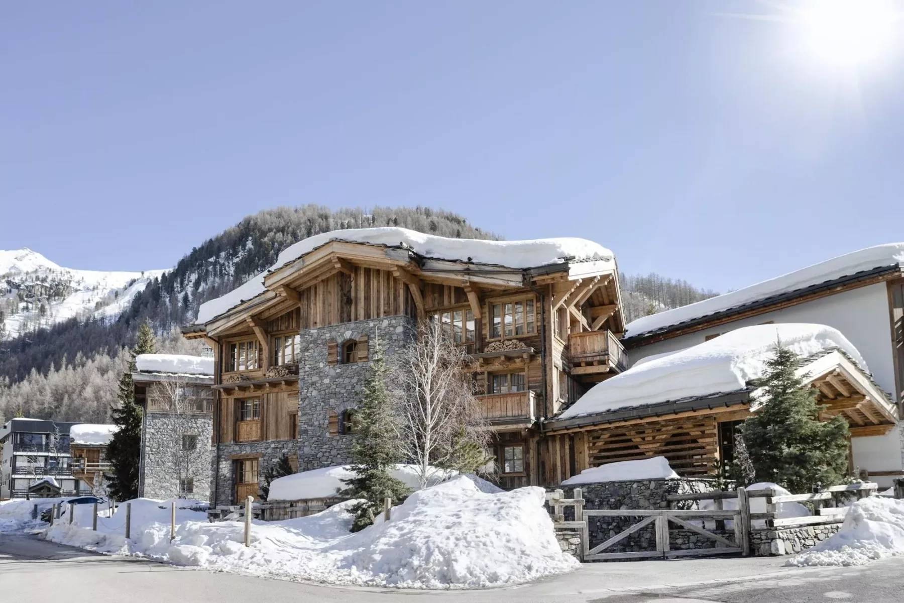 A snow-covered mountain lodge stands beside a snowy road under a clear sky.
