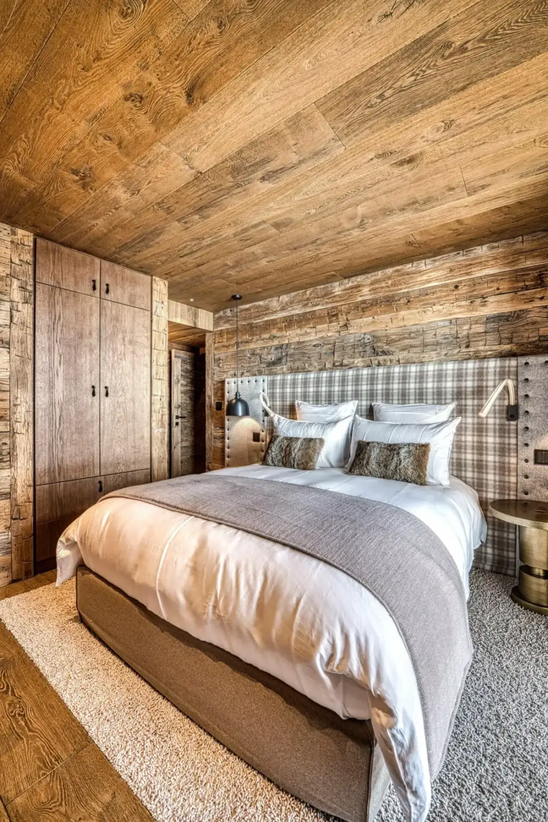 A bedroom with a large bed, patterned headboard, and wood-paneled walls.