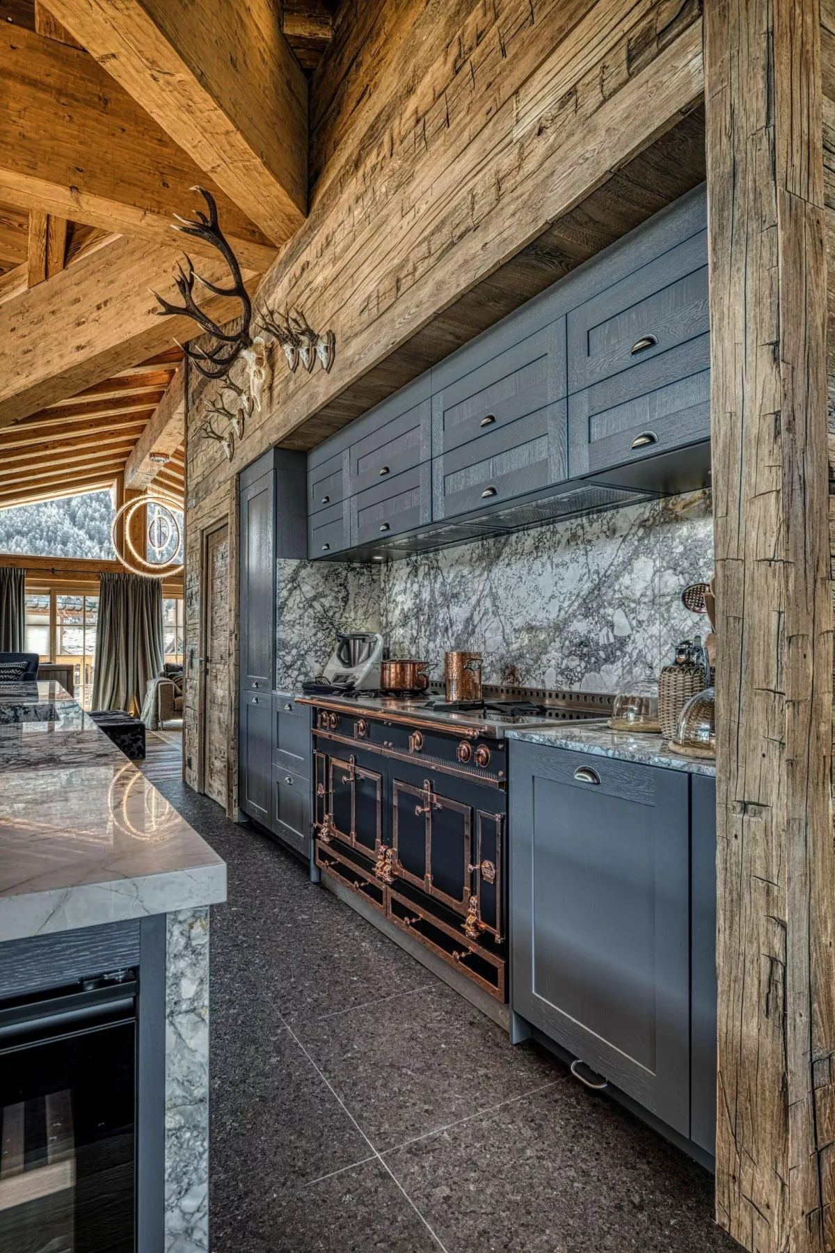 A rustic kitchen with dark cabinetry, a stone backsplash, and exposed timber beams.