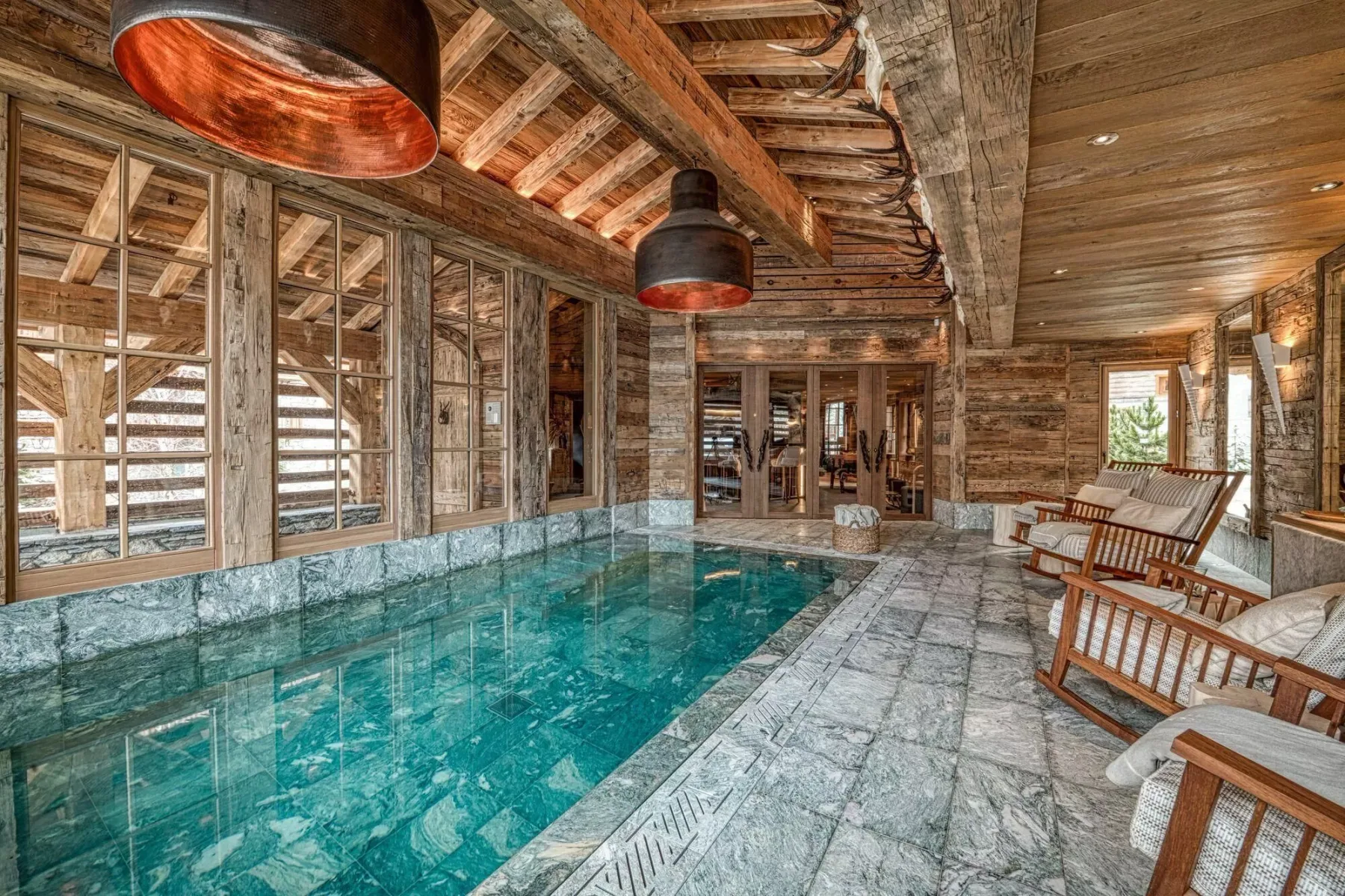 An indoor pool beneath exposed wooden beams, with seating along the side.