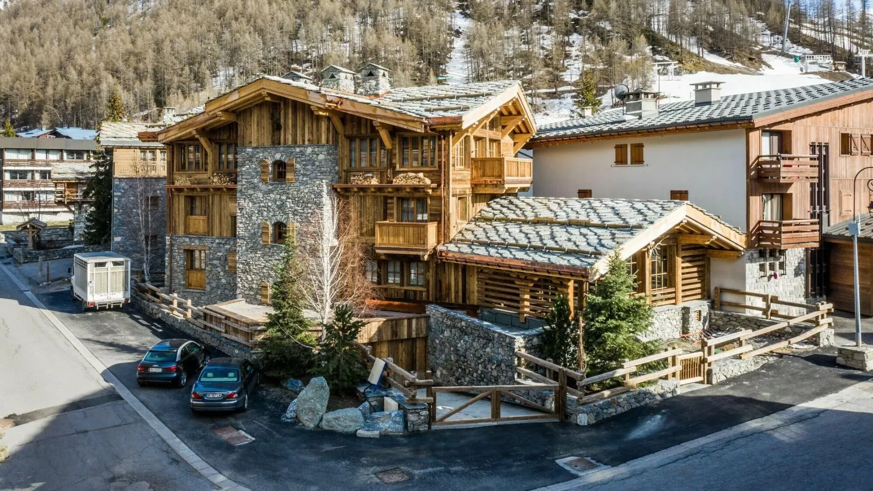 A cluster of mountain buildings with wooden balconies stands beside a snowy hillside.