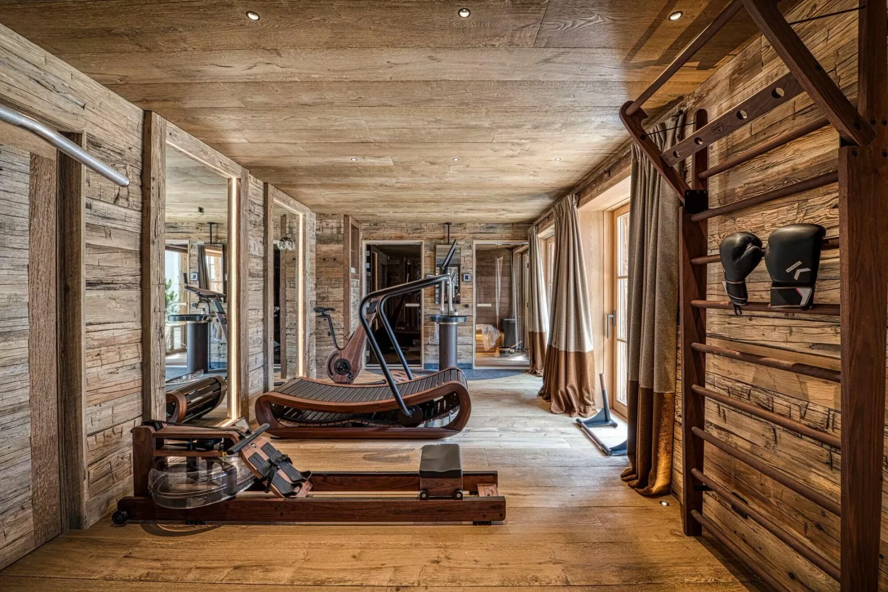 A wood-paneled exercise room with workout equipment and tall windows.