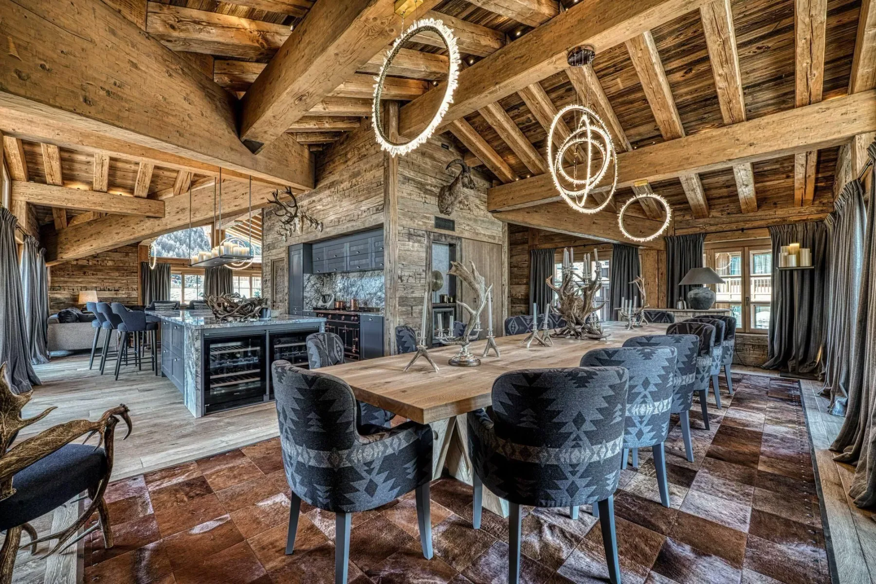 A rustic dining area with a long wooden table and upholstered seating beneath exposed timber beams.