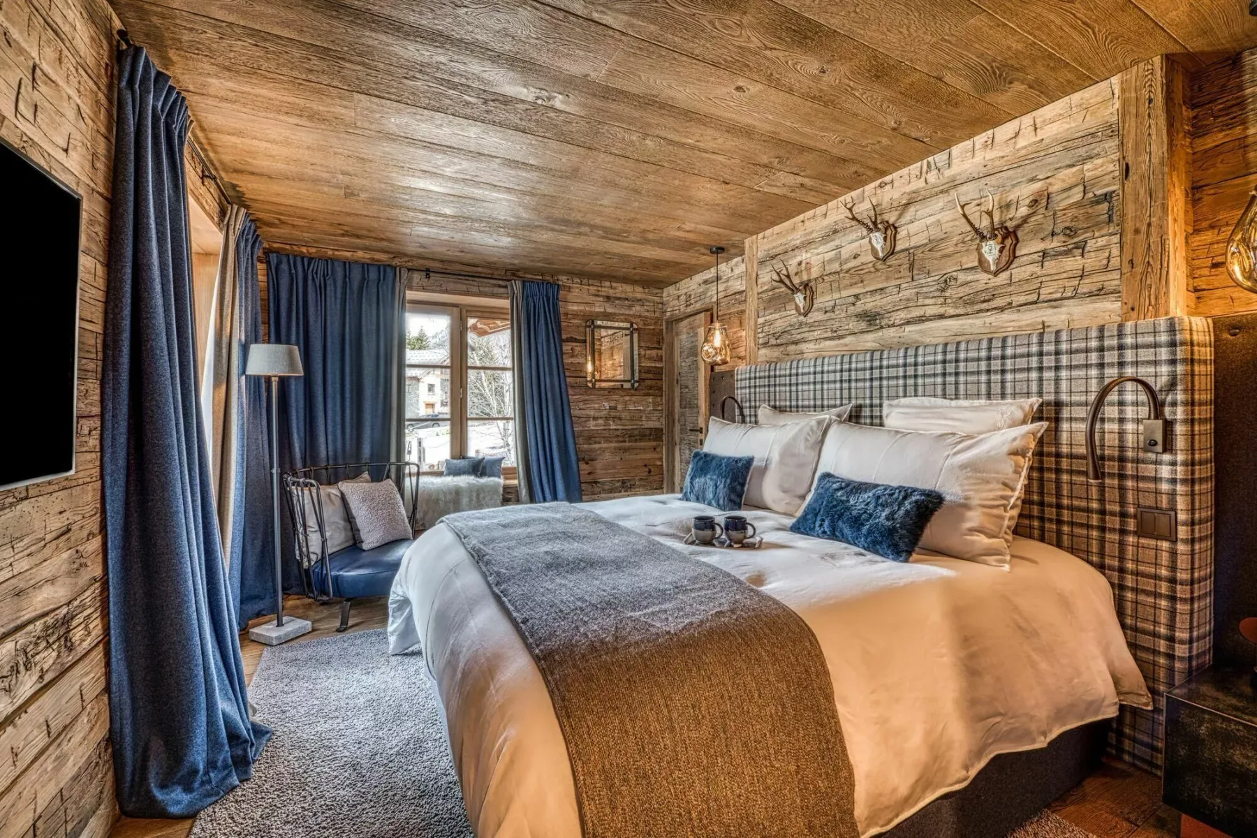 A rustic bedroom with a large bed and a window framed by blue curtains.