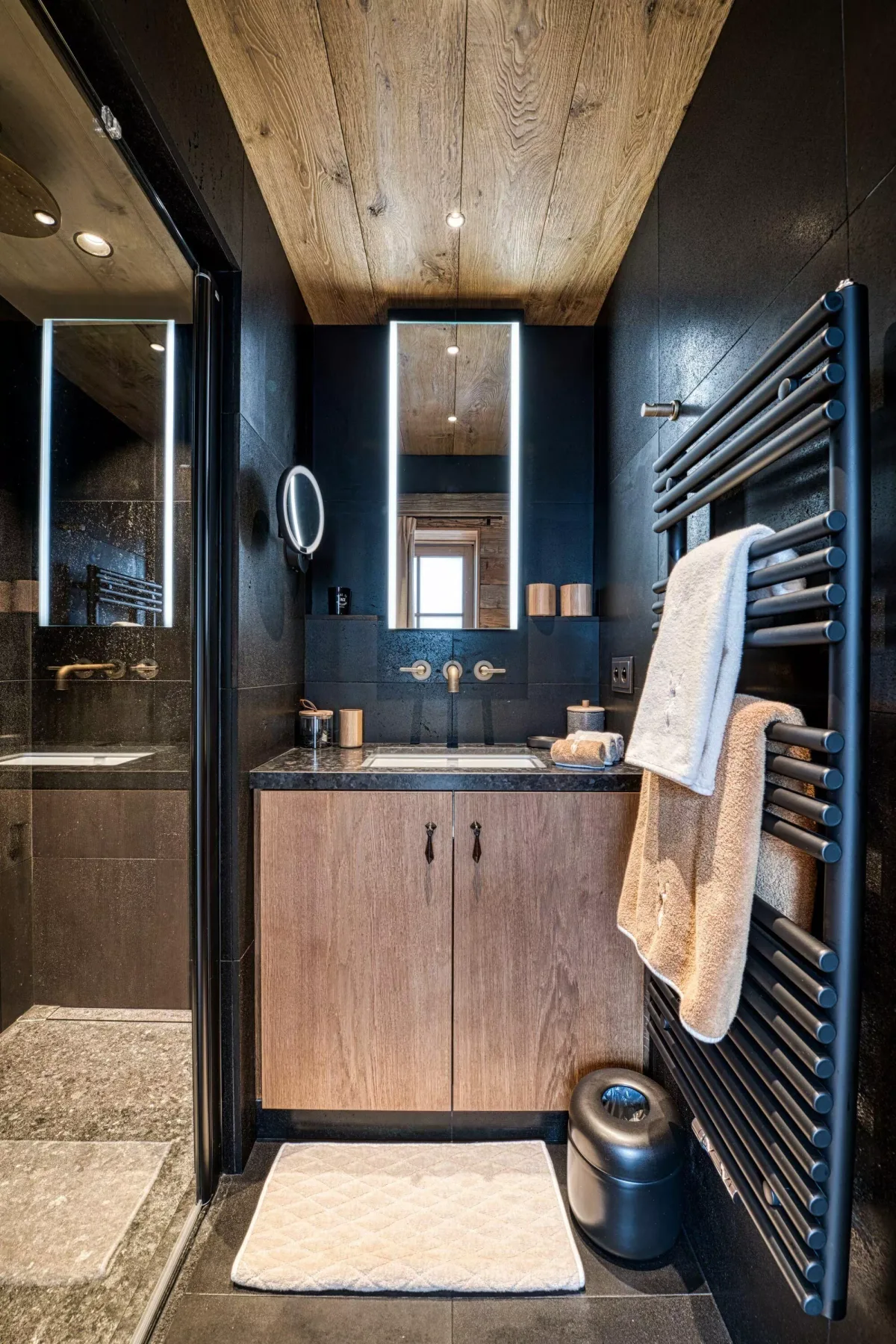 A dark bathroom with a wood vanity, mirror, and towel warmer.