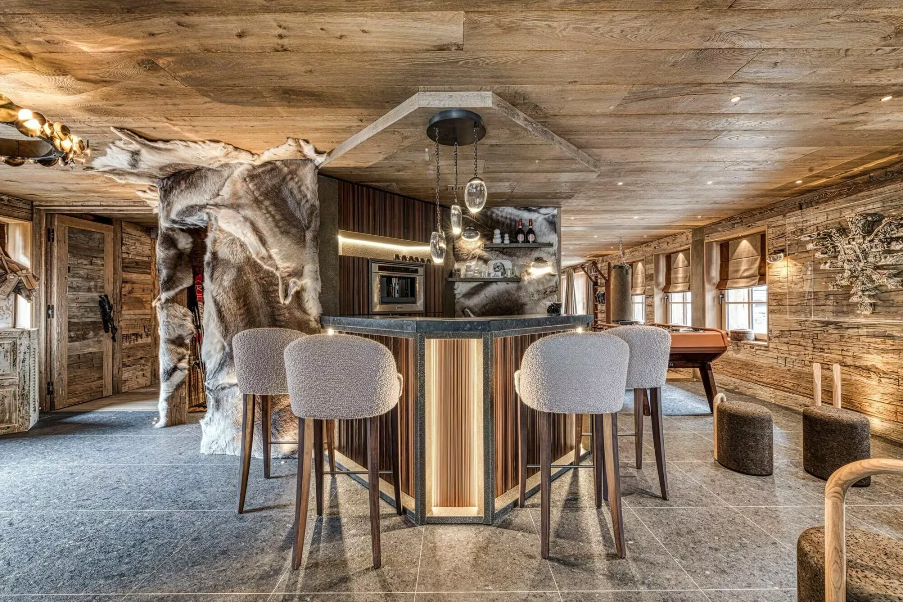 A rustic lounge with a central bar, upholstered seating, and wood-paneled surfaces.
