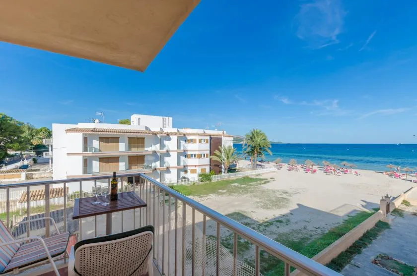 A balcony overlooks a beachfront building, sandy shore, and blue sea.