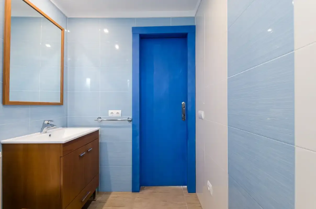 Un baño alicatado con un mueble de madera y una puerta azul.
