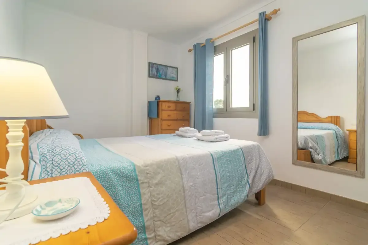 Un dormitorio con una cama bien tendida y cortinas azules junto a la ventana.