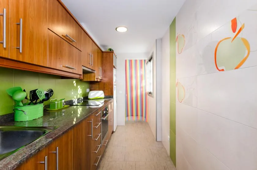 Una cocina estrecha con gabinetes de madera, una encimera y una cortina colorida al fondo.