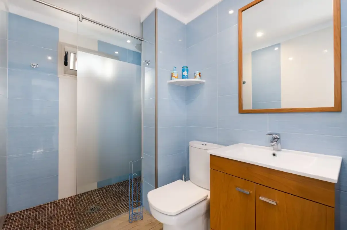 Un baño alicatado con ducha, inodoro y lavabo con mueble.