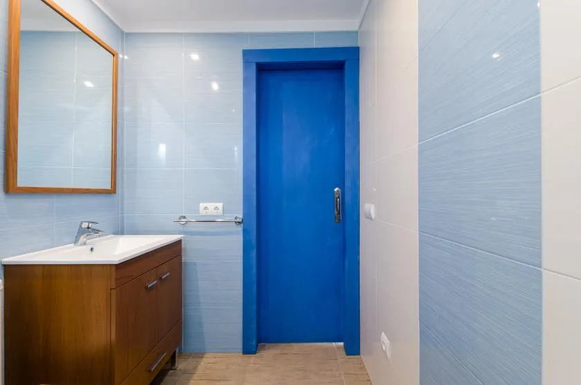 Un baño con azulejos, un mueble de madera y una puerta azul brillante.