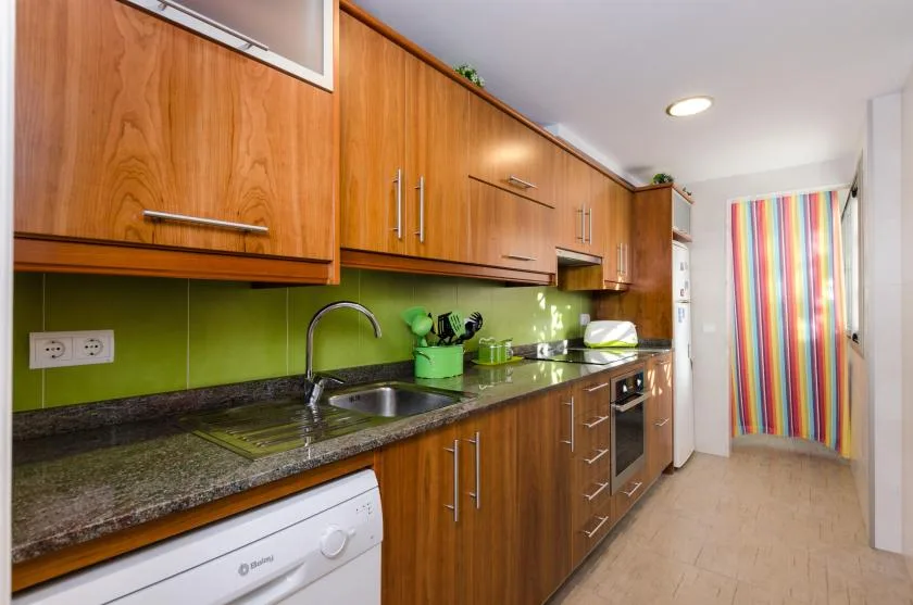 Una cocina estrecha con armarios de madera, una encimera oscura y una cortina de rayas de colores.