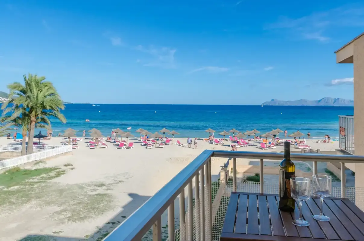 Un balcón da a una playa de arena con filas de sombrillas y el mar al fondo.